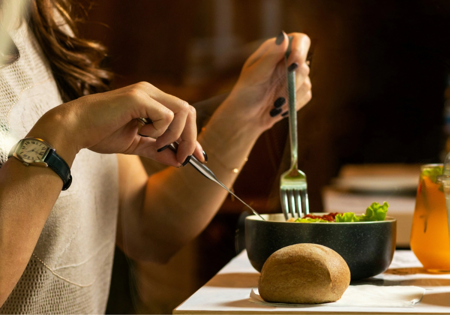 Person eating a salad with a roll and drink on the table