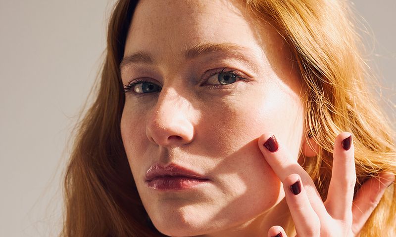 Gen Z redheaded female touching her face softly with painted nails. Beauty and wellness concept