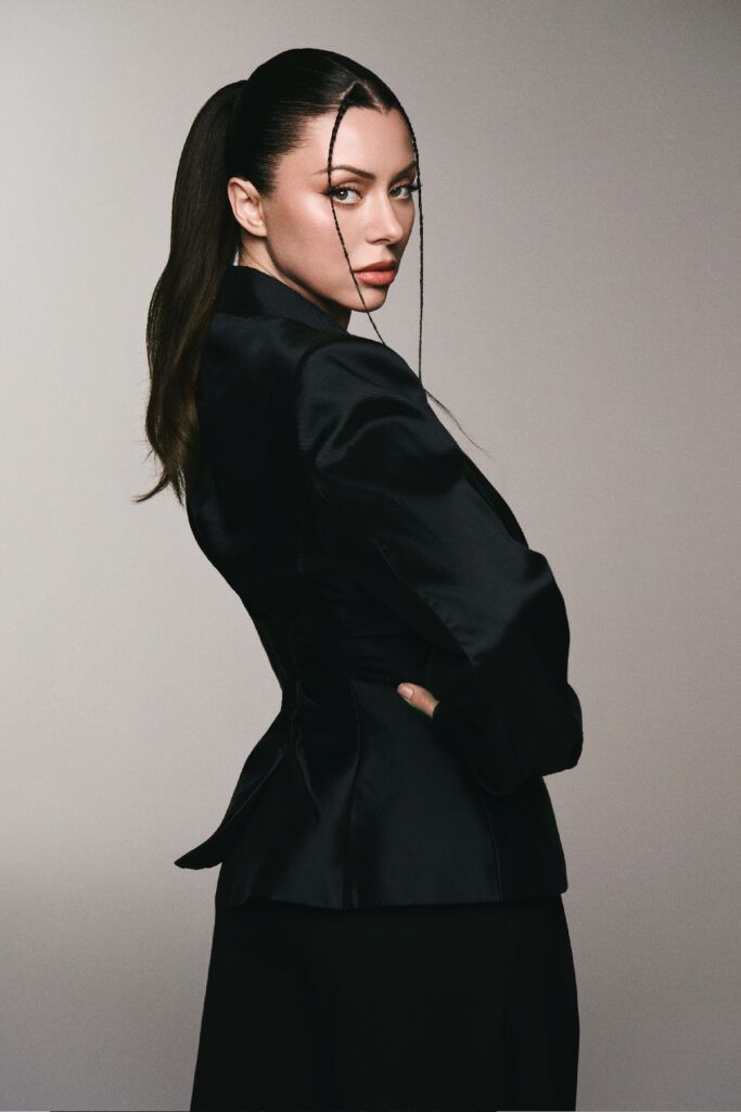 Close-up portrait of Neraida Bega in a black pinstripe suit, featuring glowing skin, defined eyes and a neutral lip