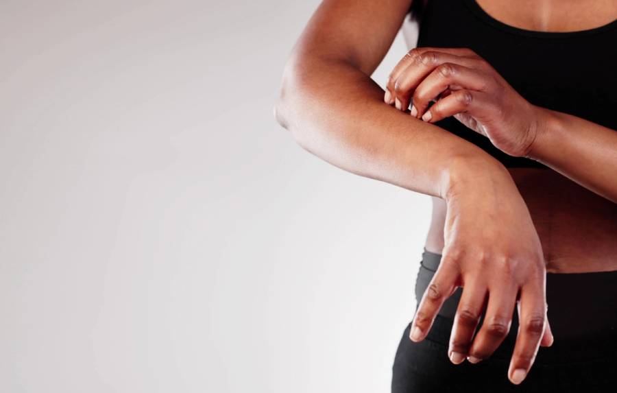A woman in black activewear scratches her forearm against a white background.