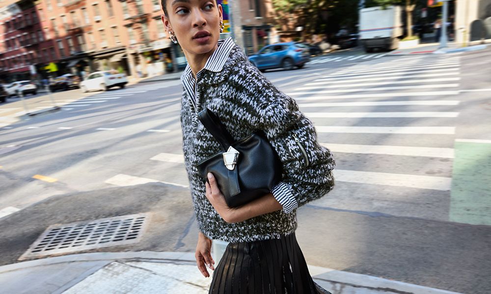 woman walking on city street with merit beauty and brandon maxwell bag