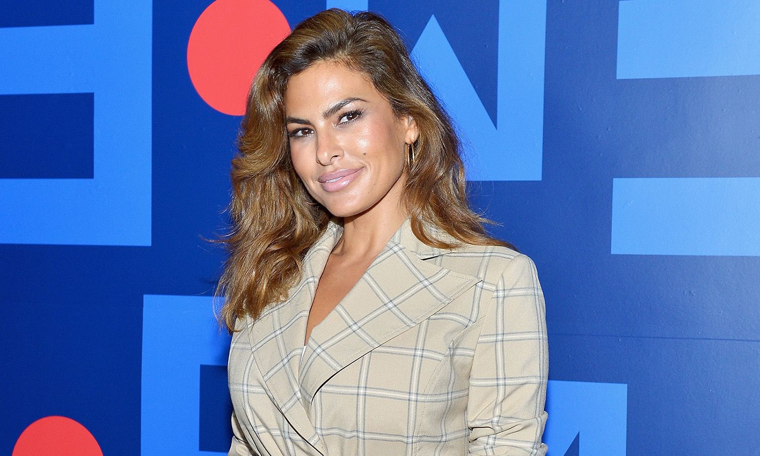 Eva Mendes in a beige plaid suit in front of a blue background