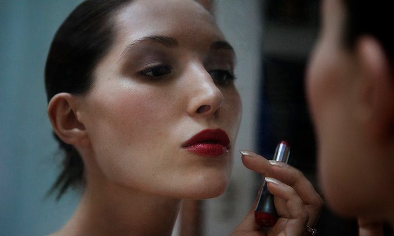 Close-up of woman looking at mirror while holding lipstick