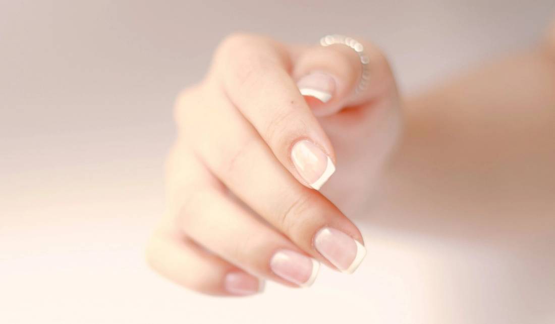 A close-up of a hand with a soft, sheer French manicure against a neutral background.