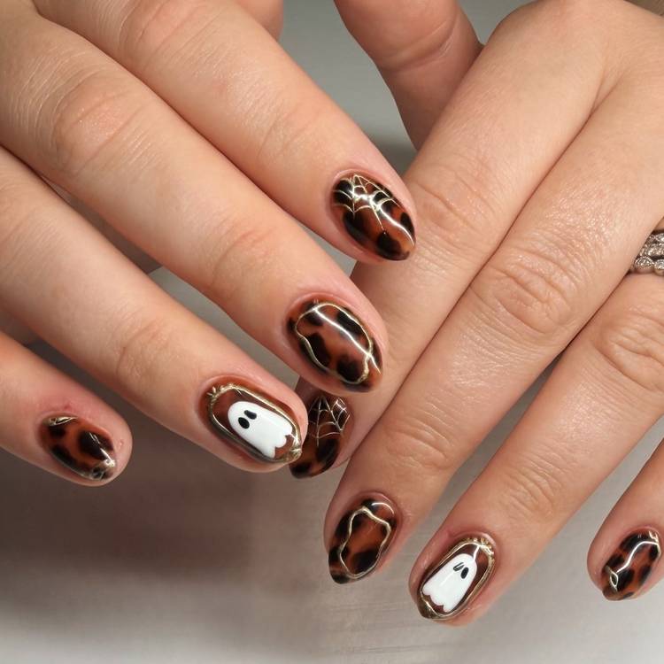 Short, rounded tortoiseshell nails with thin metallic spiderweb lines. Two accent nails have a small white ghost on a tortoiseshell base.