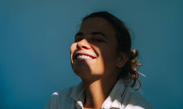 Portrait of beautiful woman on dark blue background with sun beam on face.