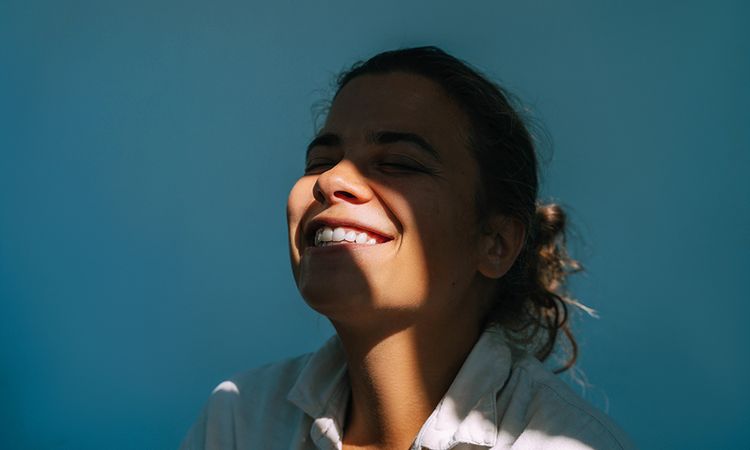 Portrait of beautiful woman on dark blue background with sun beam on face.