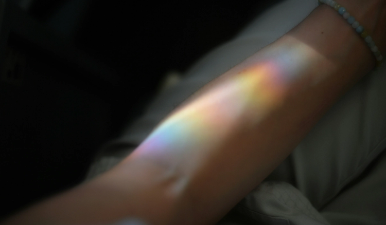 A rainbow light refraction cast across a person's forearm against a dark background