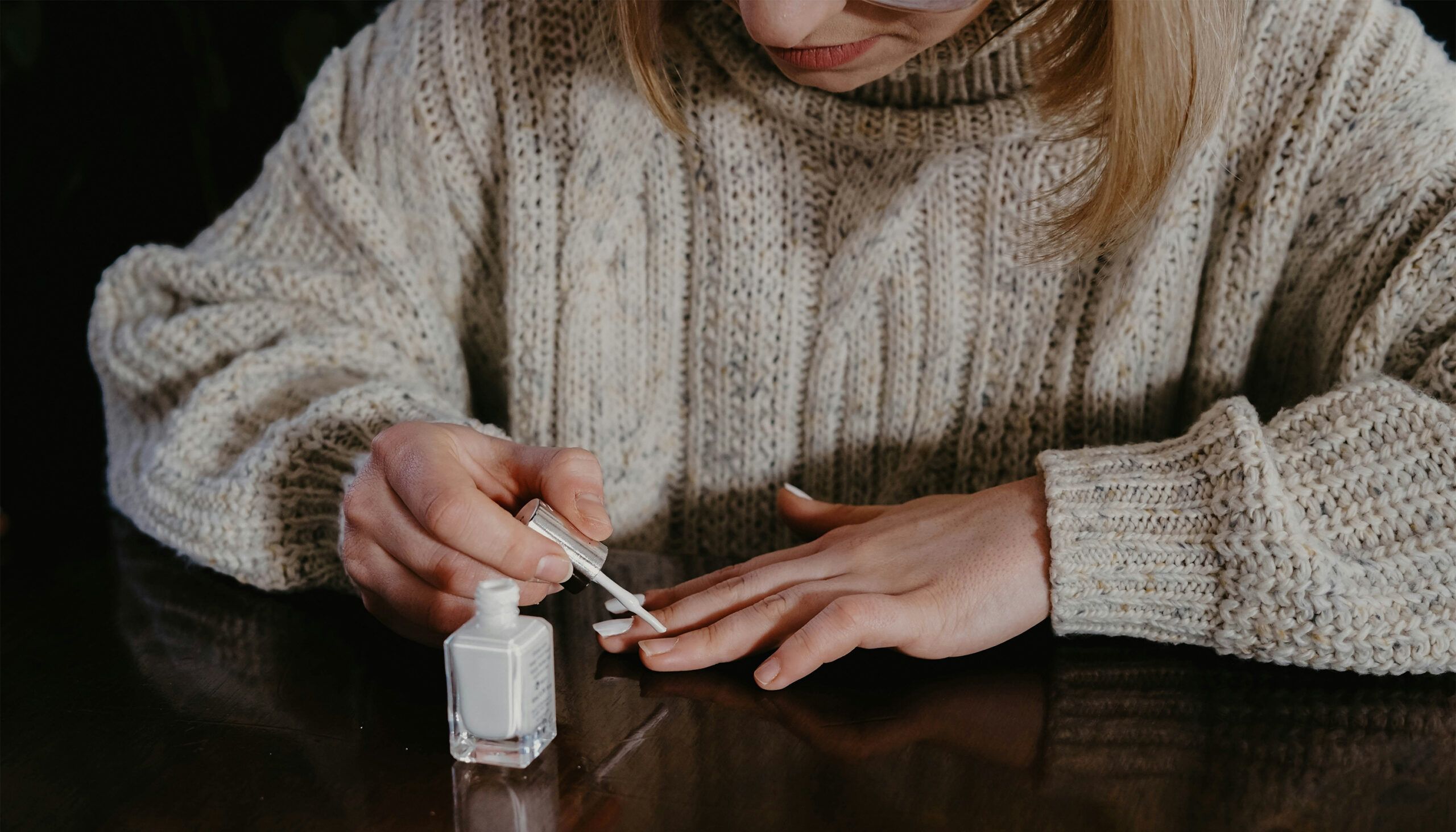 woman in a sweater painting her nails white