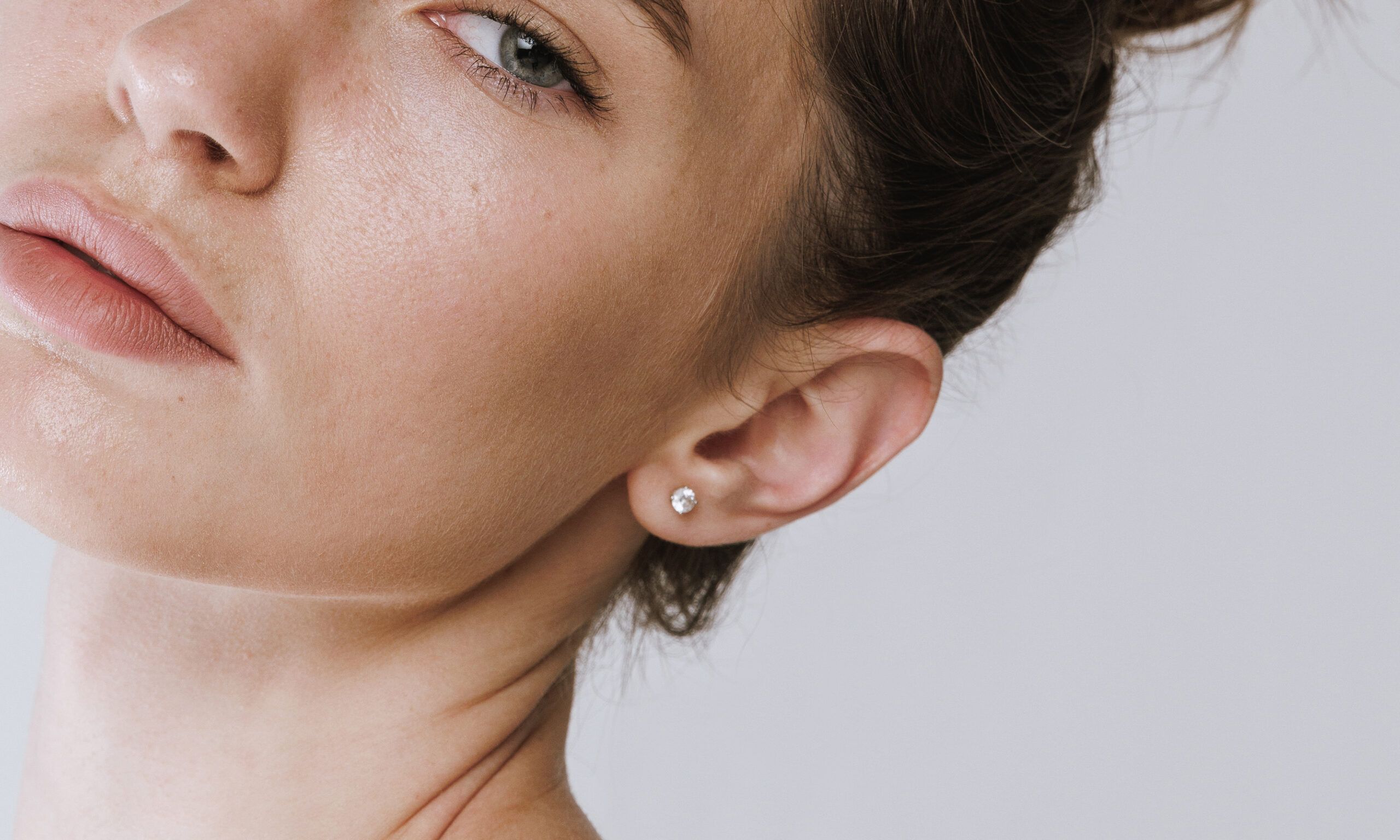 Portrait of beautiful young girl with grey eyes, natural makeup and hair bun isolated on grey studio background.