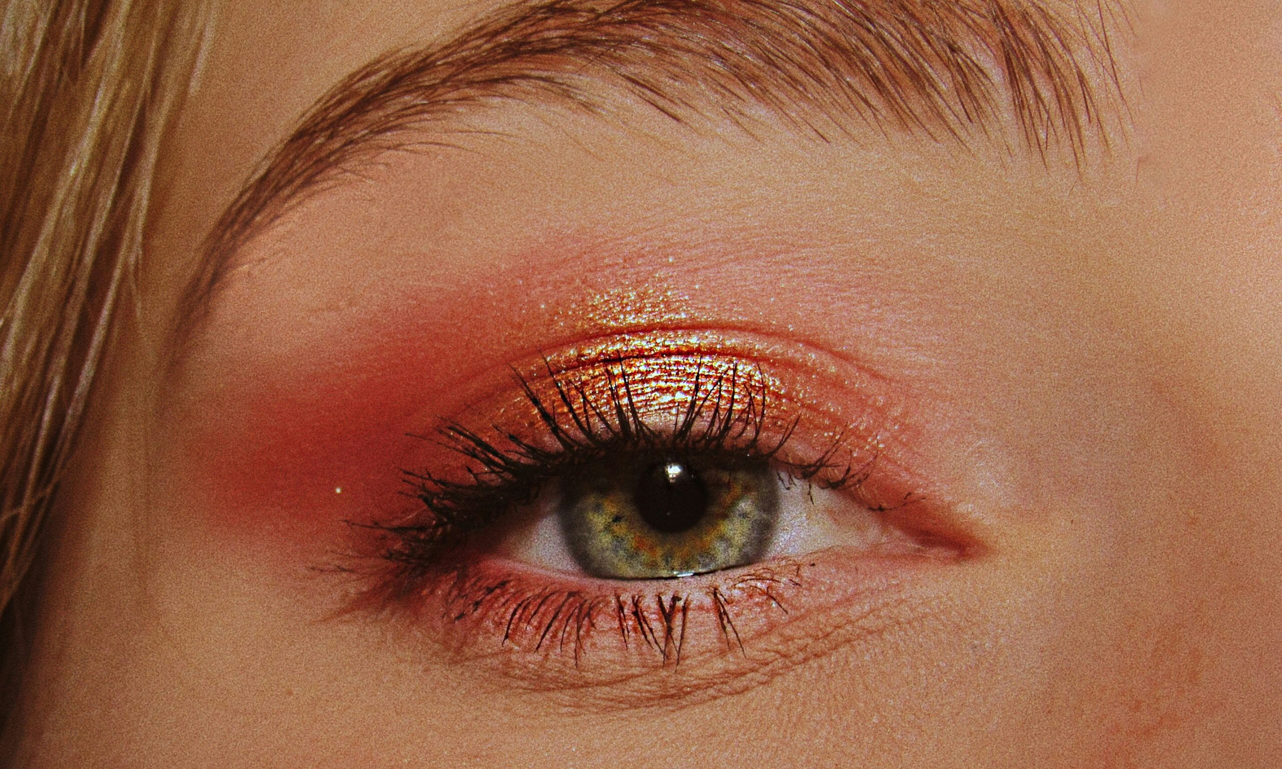 zoomed in photo of woman'e eye with red and gold eyeshadow