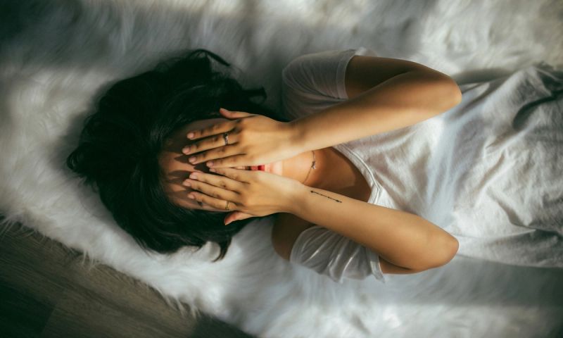 woman lying on bed with hands over her face