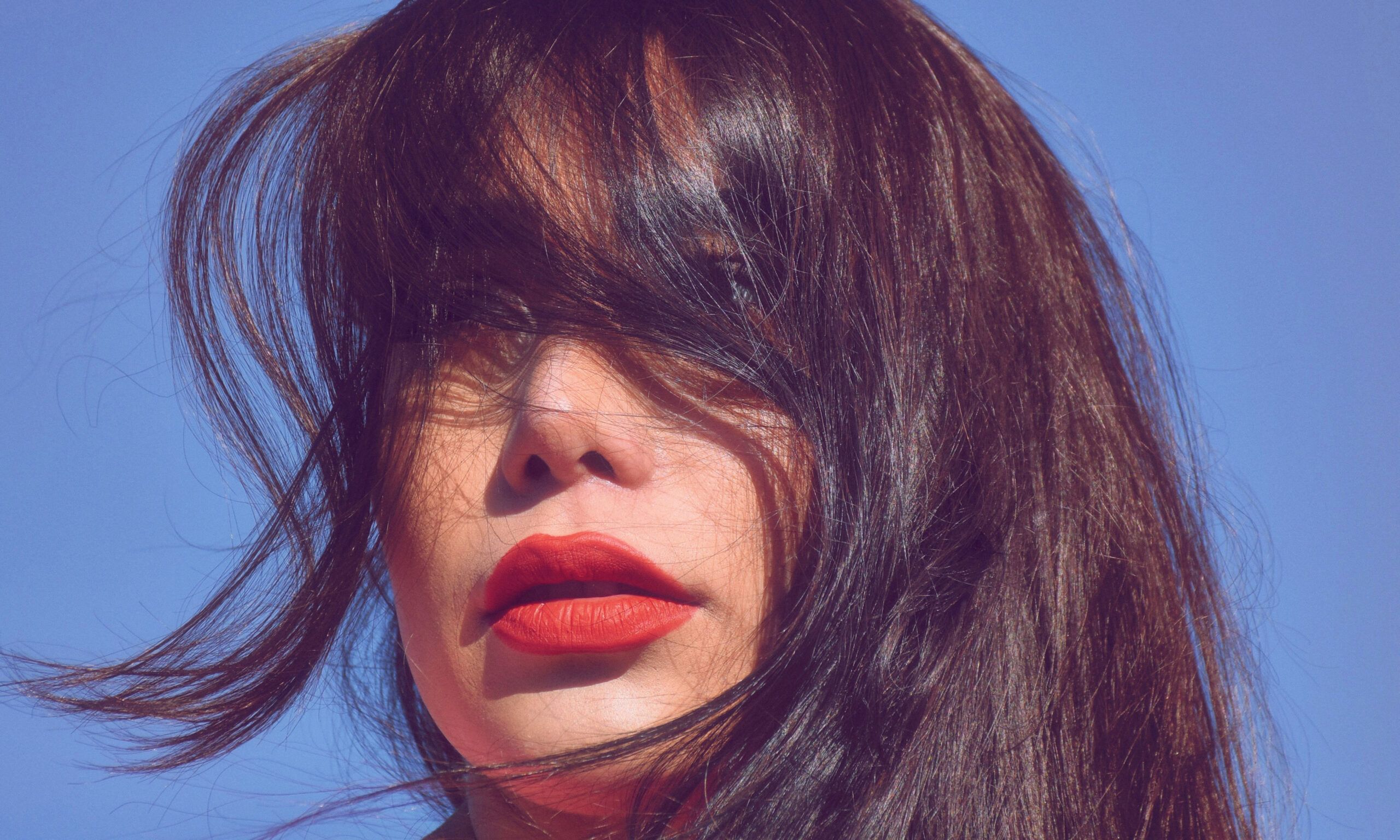 woman outdoors with bangs and hair in face wearing red lipstick