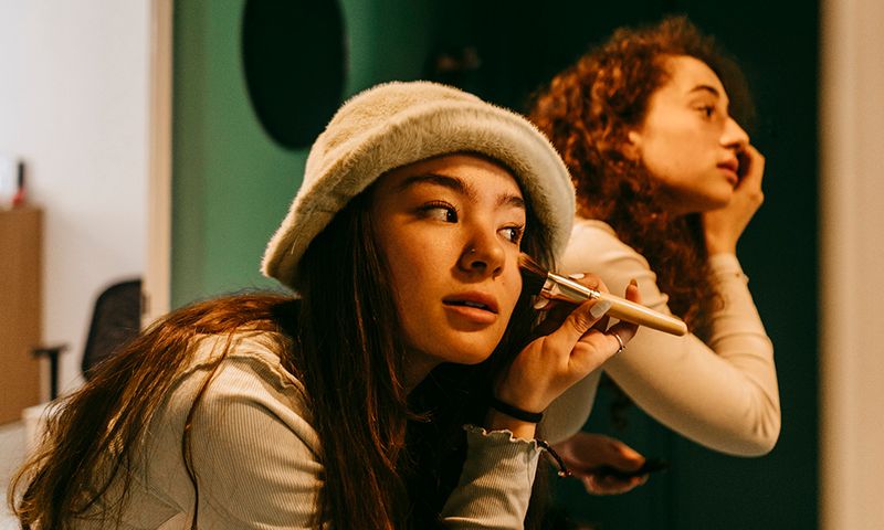 Young female friends applying make-up at home