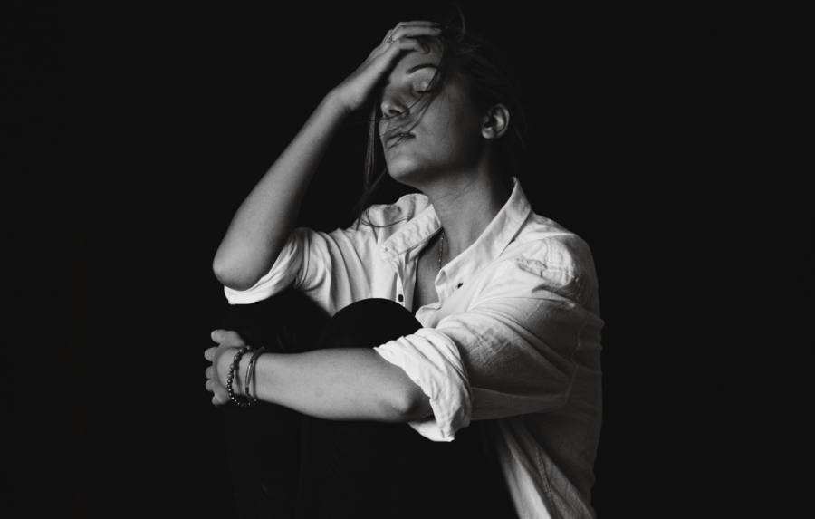 A woman sits with her head resting in her hand, photographed in black and white against a dark background