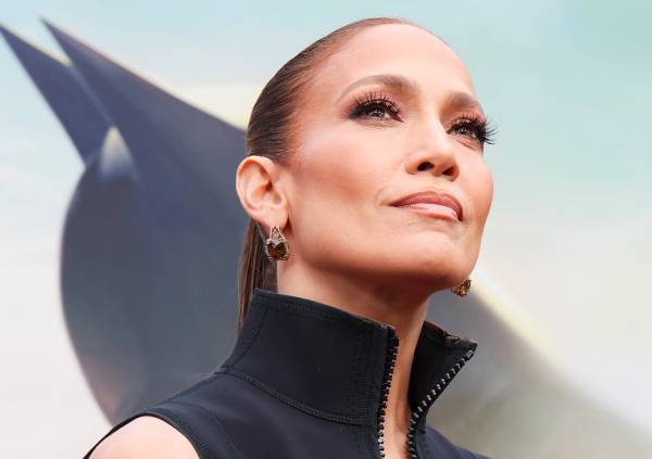 Jennifer Lopez wearing slicked-back hair, glowing makeup, statement earrings and a black high-neck top at an outdoor event.