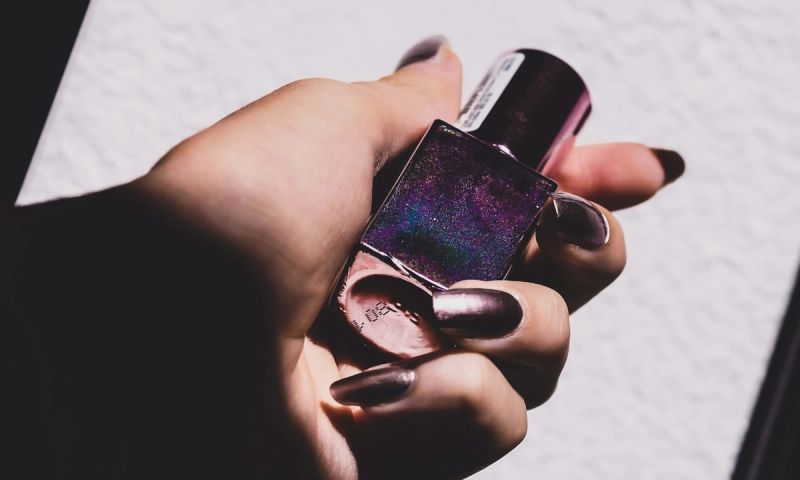 manicured hand holding purple glitter nail polish