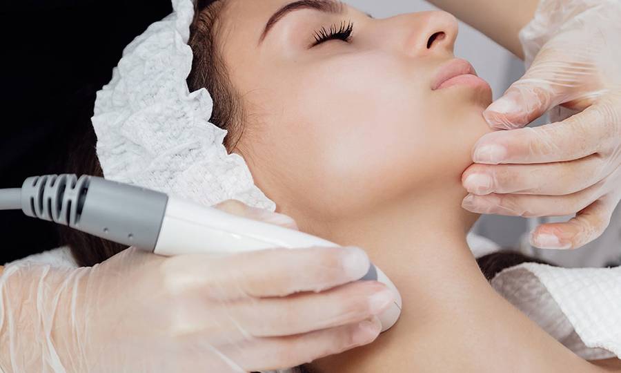young woman doctor beautician doing hardware procedure on patient's face