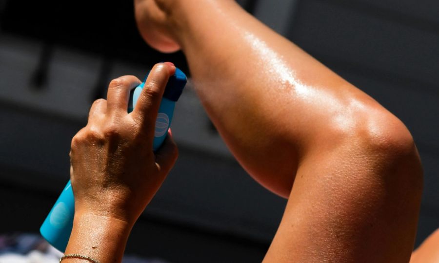 woman spraying sunscreen on leg