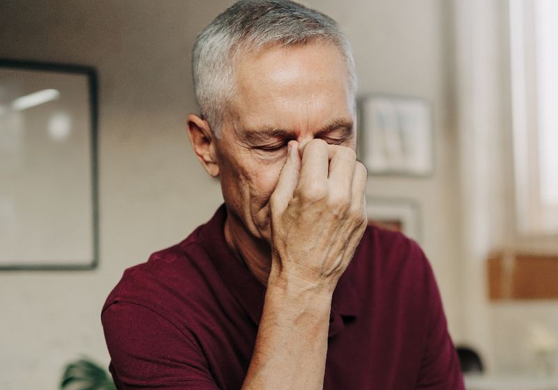 Older man touching the bridge of his nose while sitting at a laptop, illustrating nasal skin concerns such as rhinophyma.