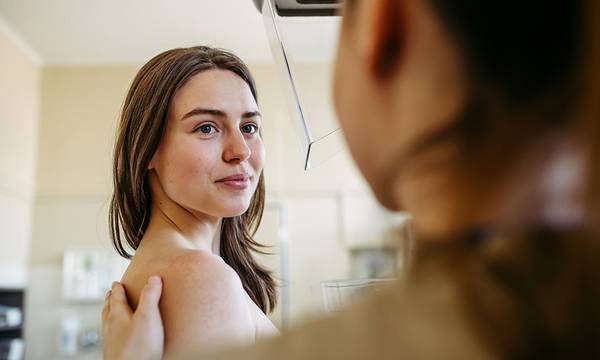 Healthcare worker talking with female patient during mammogram screening.