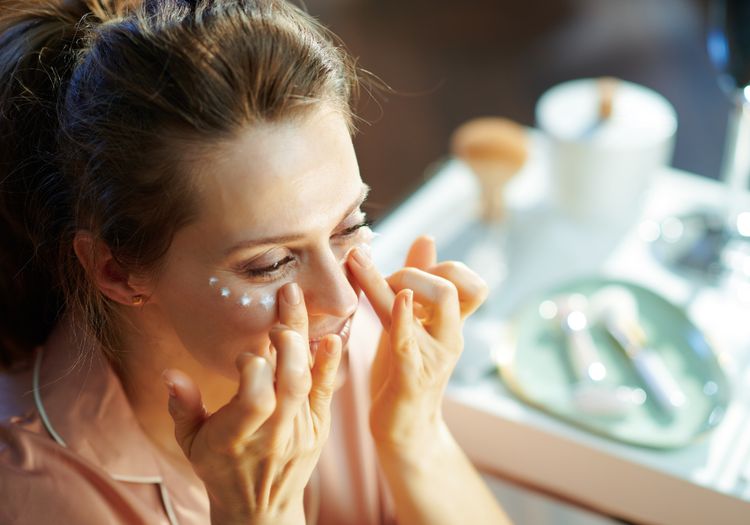 Woman applying under-eye cream beneath both eyes in a well-lit setting