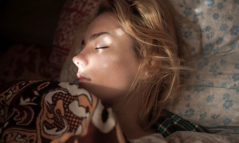 close up of blonde woman sleeping in bed with sunlight on face