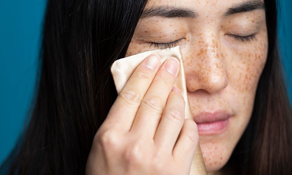 Woman with eyes closed cleaning face against blue background