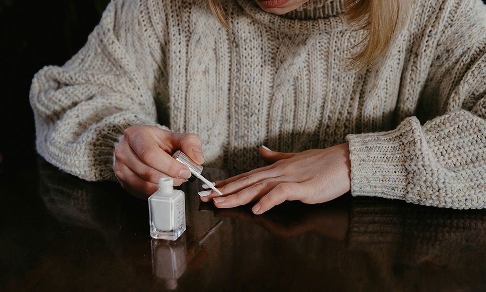 woman painting her nails with white nail polish at a table