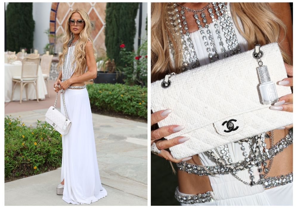 Rachel Zoe in a white embellished gown and layered silver jewelry, holding a white Chanel clutch with a miniature Essie nail polish charm attached, showcasing her neutral-toned manicure following her appointment as Essie’s Chief Color Director.