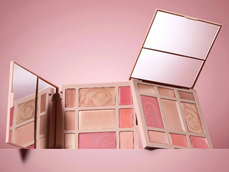 Laura Geller baked face palettes featuring blush, highlighter and eyeshadow in soft pink and bronze tones, displayed against a blush-toned background with open mirrors.