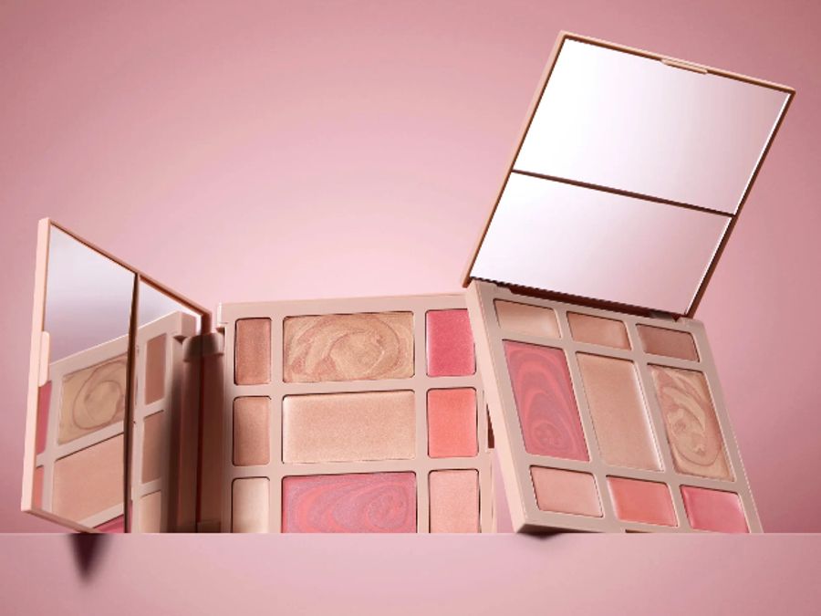 Laura Geller baked face palettes featuring blush, highlighter and eyeshadow in soft pink and bronze tones, displayed against a blush-toned background with open mirrors.