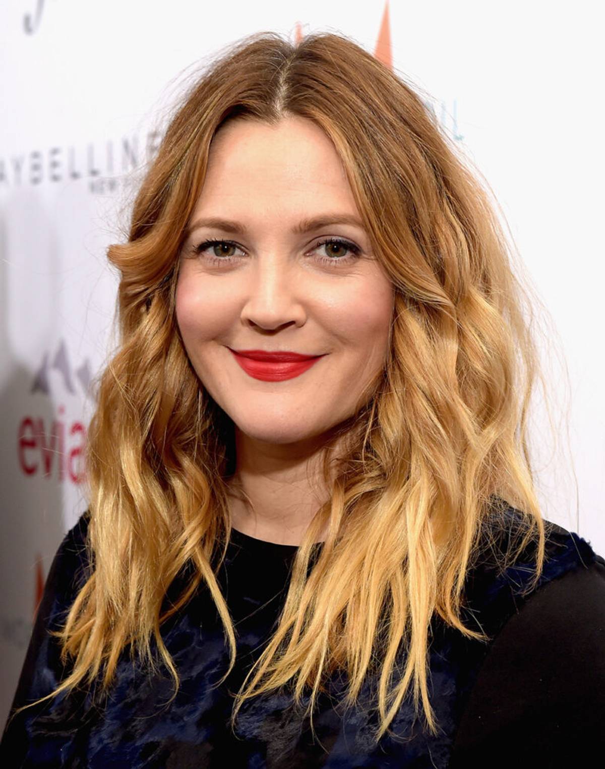 Actress Drew Barrymore wearing a black dress with red lipstick, blonde wavy hair.