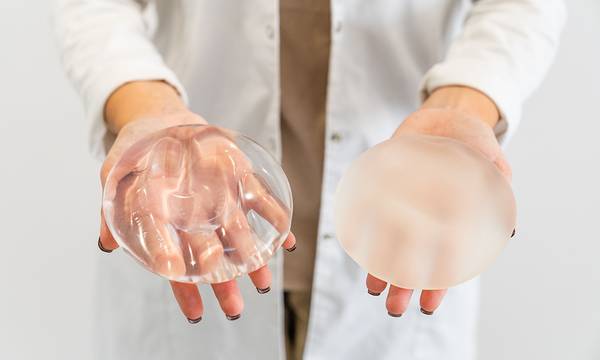 The Doctor's hands holding two different types of breast prostheses.