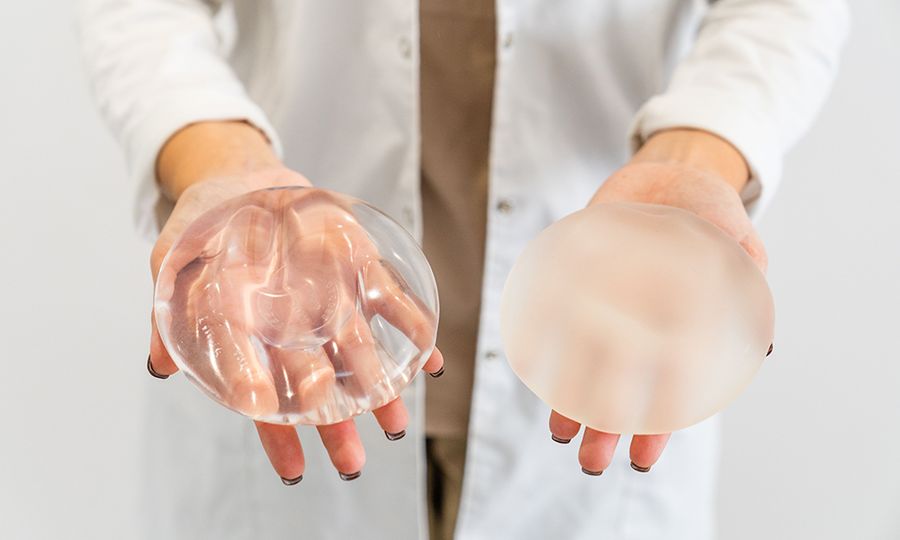 The Doctor's hands holding two different types of breast prostheses.