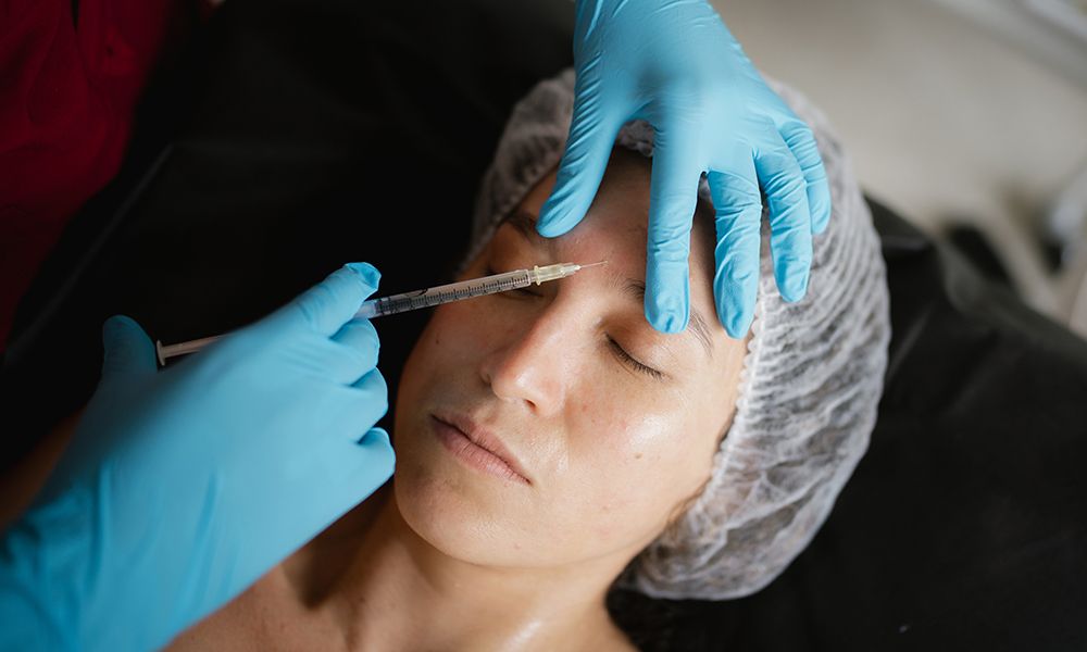 Doctor injecting botulinum toxin into a young woman's forehead, enhancing facial rejuvenation and addressing fine lines and wrinkles