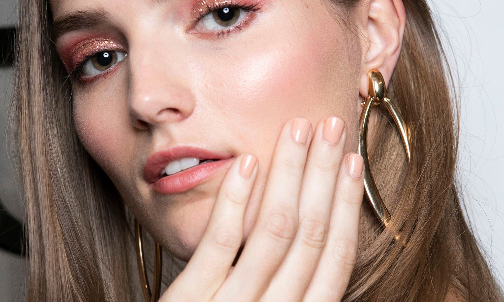 model with nude nail polish manicure touching her cheek