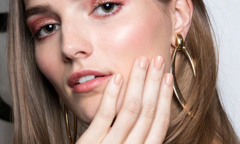 model with nude nail polish manicure touching her cheek