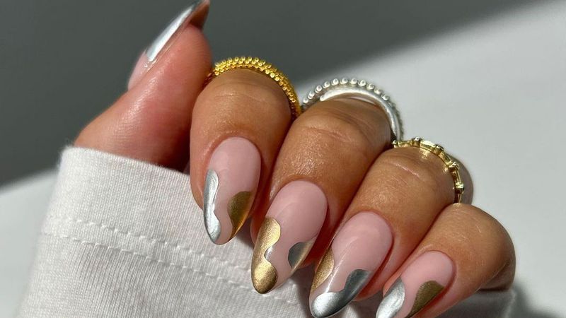 a close up of a woman's hand with a manicure with gold and silver nail design and three rings on her fingers