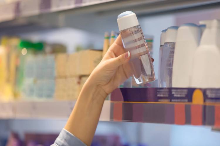 A shopper’s hand picks up a clear bottle with a white cap from a store shelf.