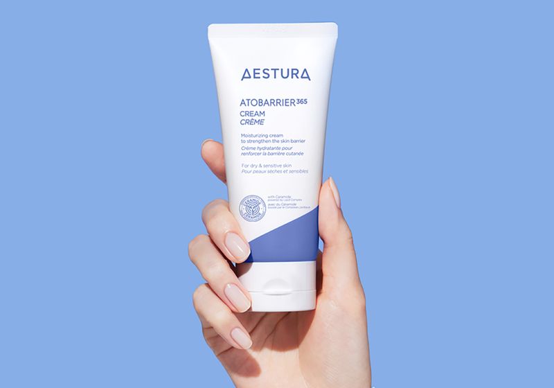 AESTURA ATOBARRIER365 Cream moisturizing barrier cream in a white and blue tube held in hand against a light blue background.