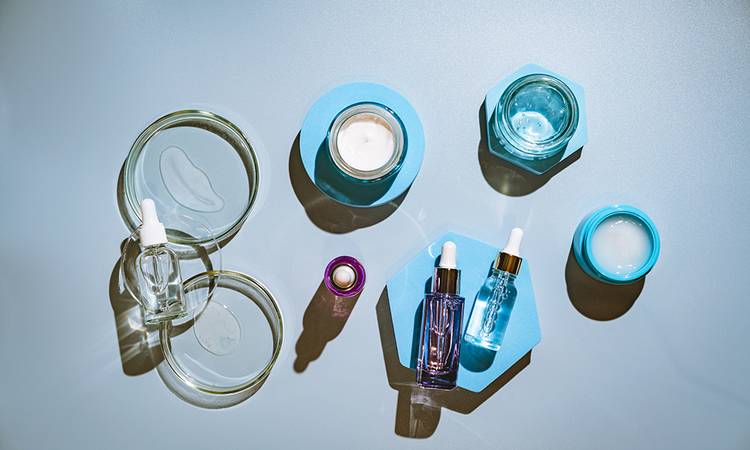 Different glass bottles with serum or oil and cosmetic skin care cream on blue background. Trending shadow. Cosmetic mockup. Top view with copy space. Flat lay.
