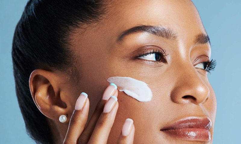 woman against blue background with moisturizer on cheek