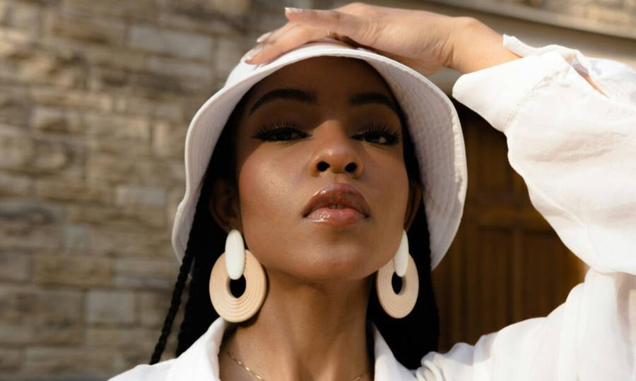 Black woman outdoors wearing a white hat and large earrings