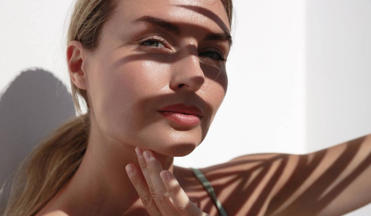 Woman with palm-leaf shadows on her face touching her fingers to her jawline