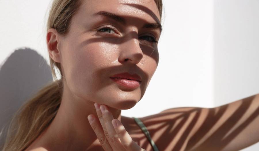 Woman with palm-leaf shadows on her face touching her fingers to her jawline