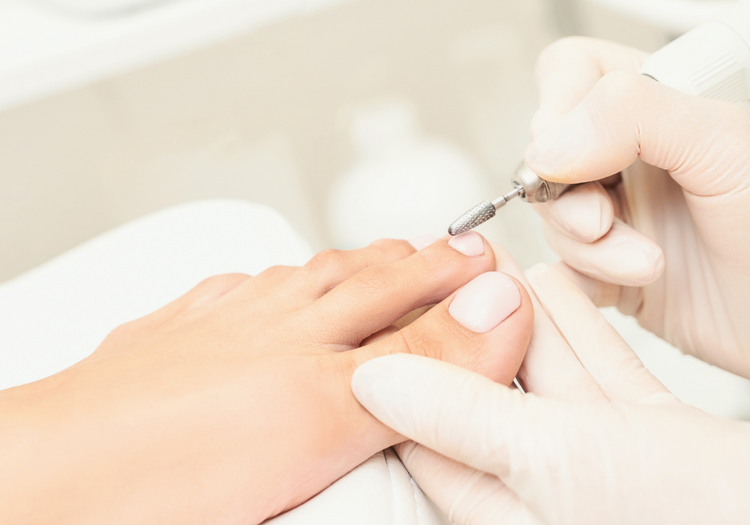 Close-up of a medical pedicure treatment being performed with an electric nail drill during a clinical foot-care appointment.