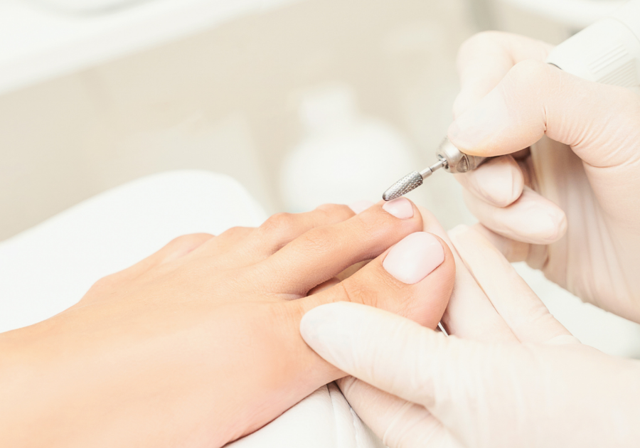 Close-up of a medical pedicure treatment being performed with an electric nail drill during a clinical foot-care appointment.