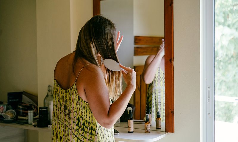 A beautiful middle-aged woman in a dress combing hair with a comb in the bathroom near the mirror. Daily morning routine, facial skin care, home treatment. A room in a luxury hotel, business trip or vacation in a high class apartment. Relaxation, mindfulness and zen-like