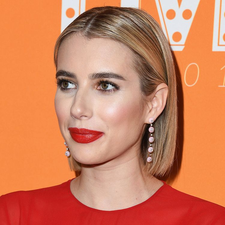 Emma Roberts with a short bob hairstyle posing on the red carpet in red dress and red lipstick